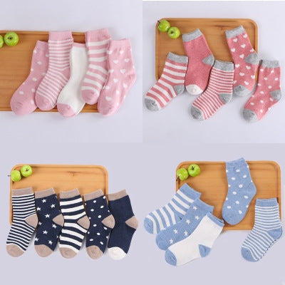 Set of children's socks in pink, blue, and white on a wooden board with green apples.