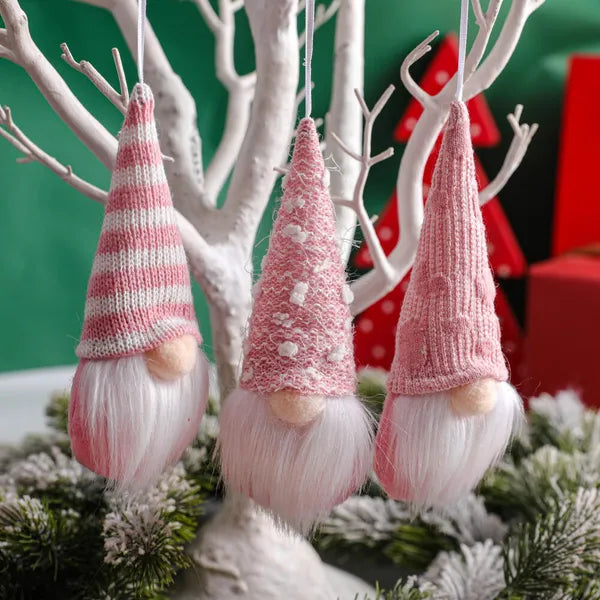 Three pink knitted gnome ornaments hanging from branches with a festive background.