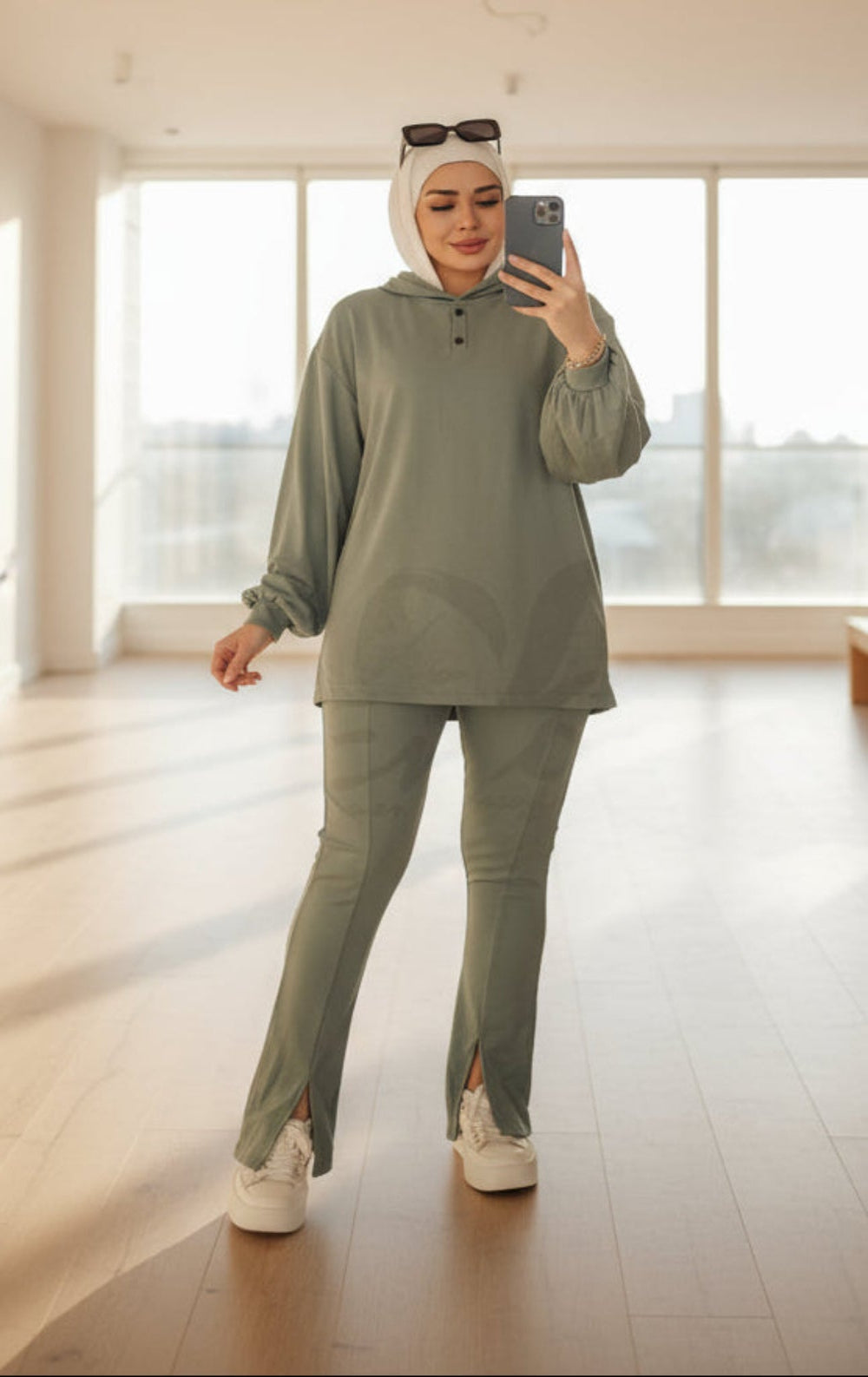 Woman taking a mirror selfie wearing a green outfit with 'Emo' branding in the background.