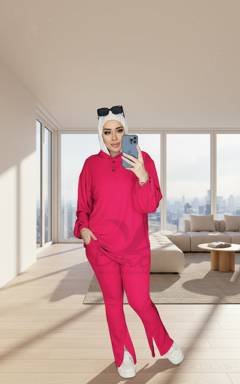 Person wearing a bright pink outfit taking a mirror selfie in a room with a visible brand logo.