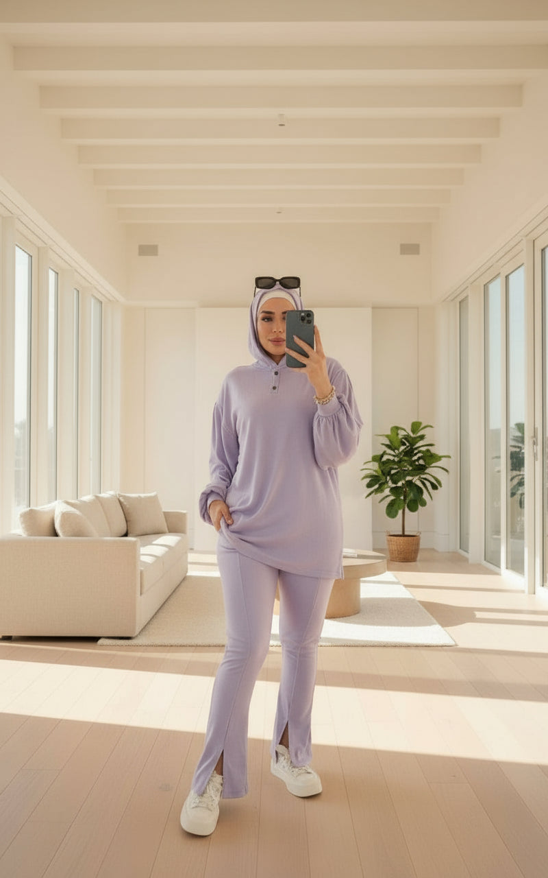 Person taking a mirror selfie in a modern living room wearing a lavender outfit.